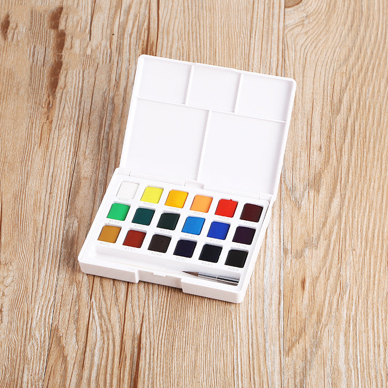 Set of watercolor paints in a white case on a wooden surface