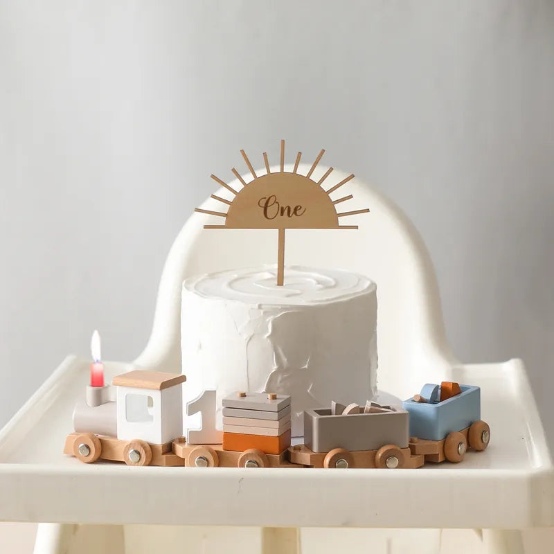 White cake with wooden train and decorations on a high chair against a plain background