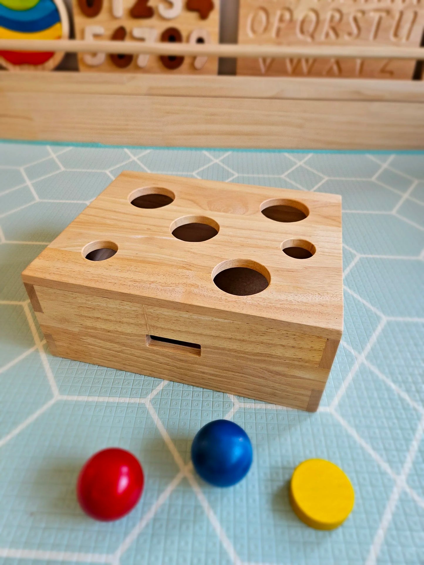 Wooden box with holes and colorful balls on a light blue grid background