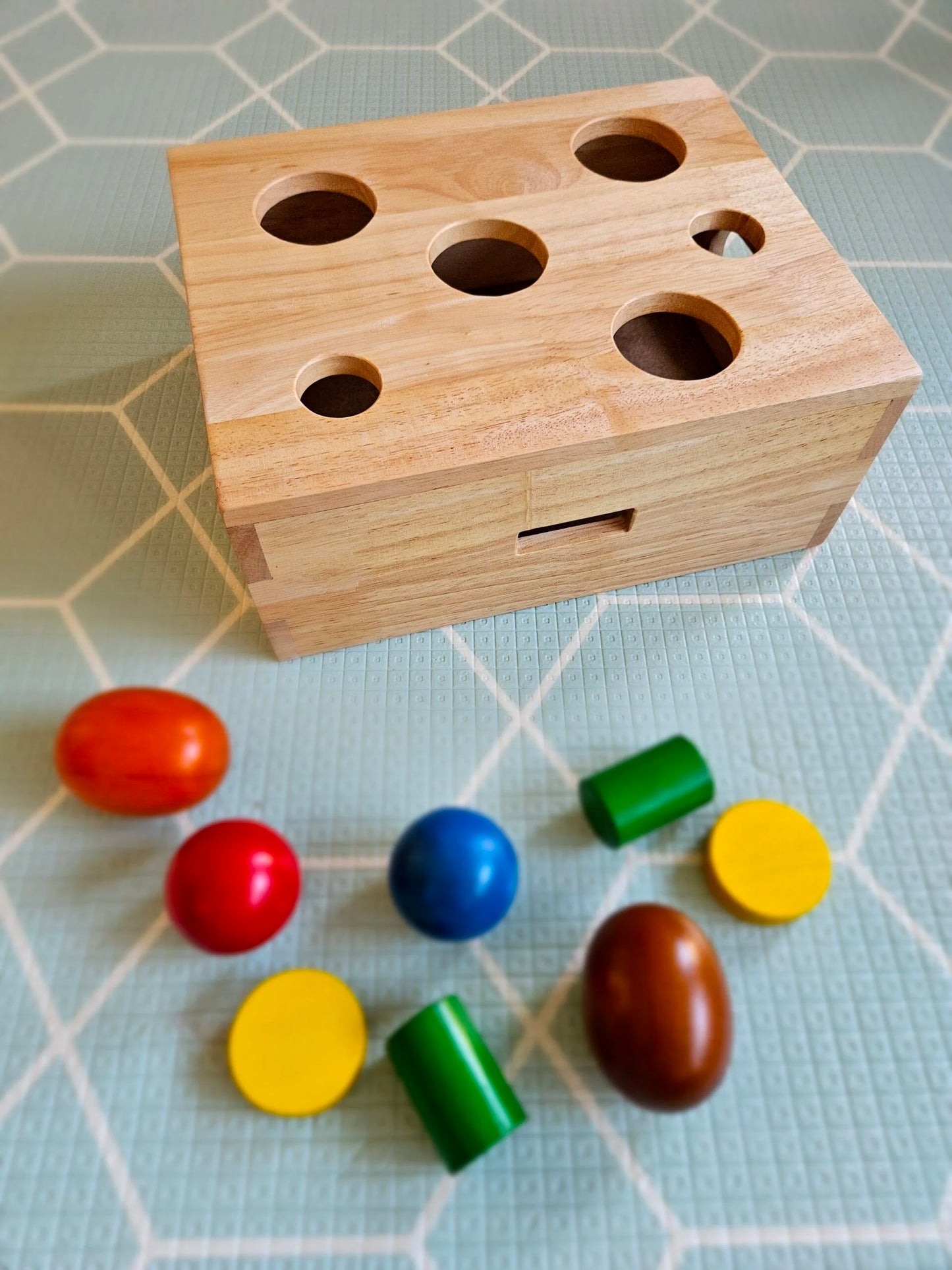 Wooden box with holes and colorful cylindrical blocks on a checkered background