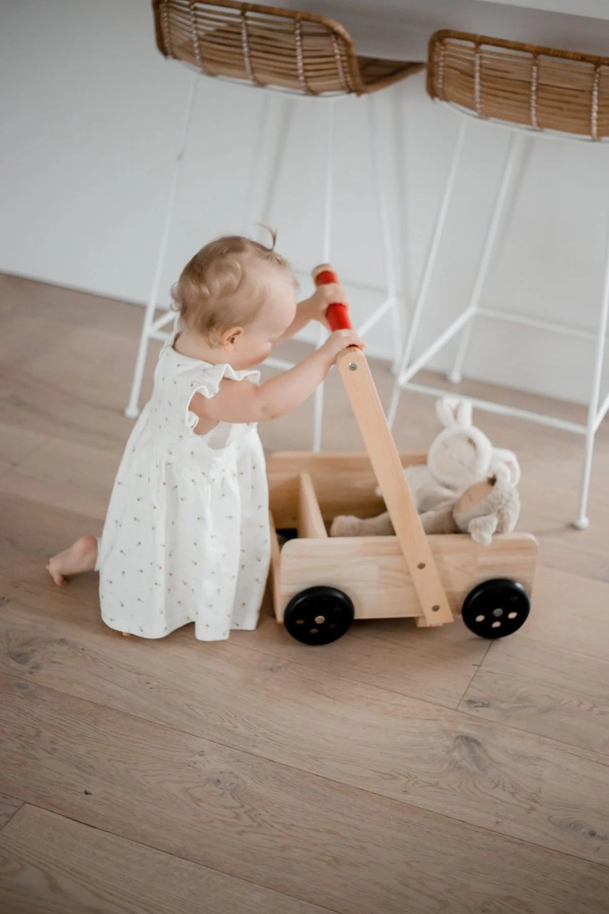 Child playing with a wooden toy cart on a wooden floor.