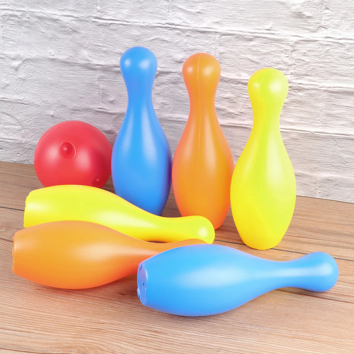 Colorful plastic bowling pins and ball on a wooden surface with a light gray background