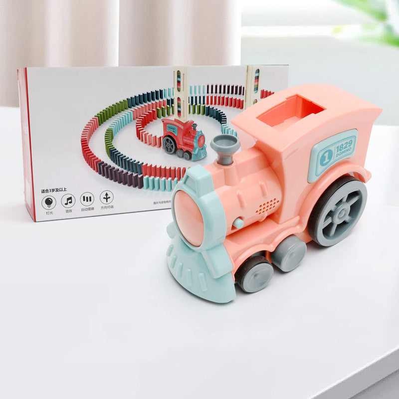 Toy train set with pink engine and green wheels on a white surface, box in the background.