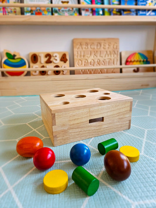 Wooden educational toy with colorful cylindrical blocks on a checkered surface, with more toys in the background.