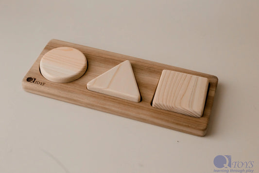 Wooden toy with geometric shapes on a wooden tray against a plain background