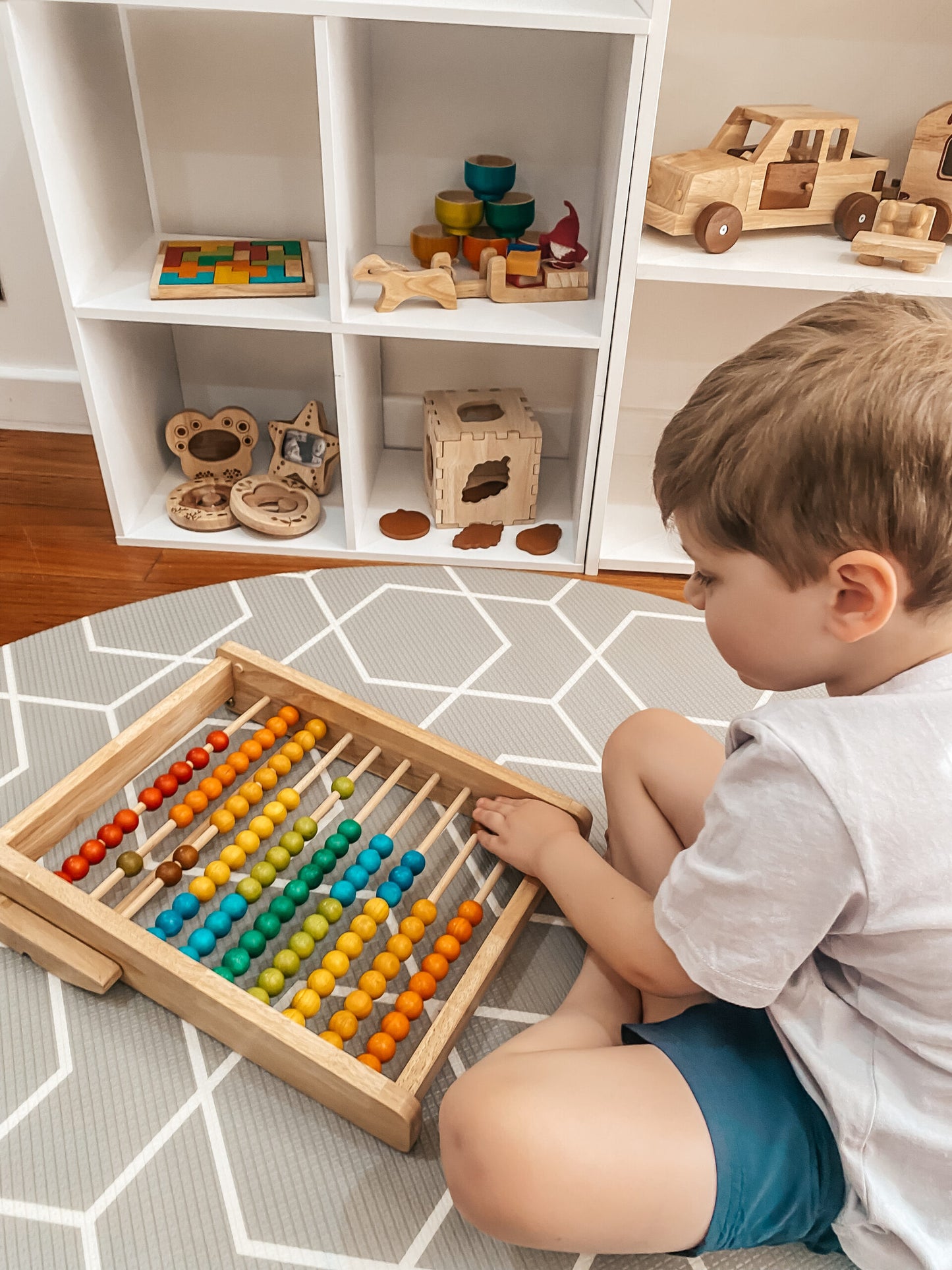 Child playing with a wooden abacus on a patterned floor with shelves in the background.