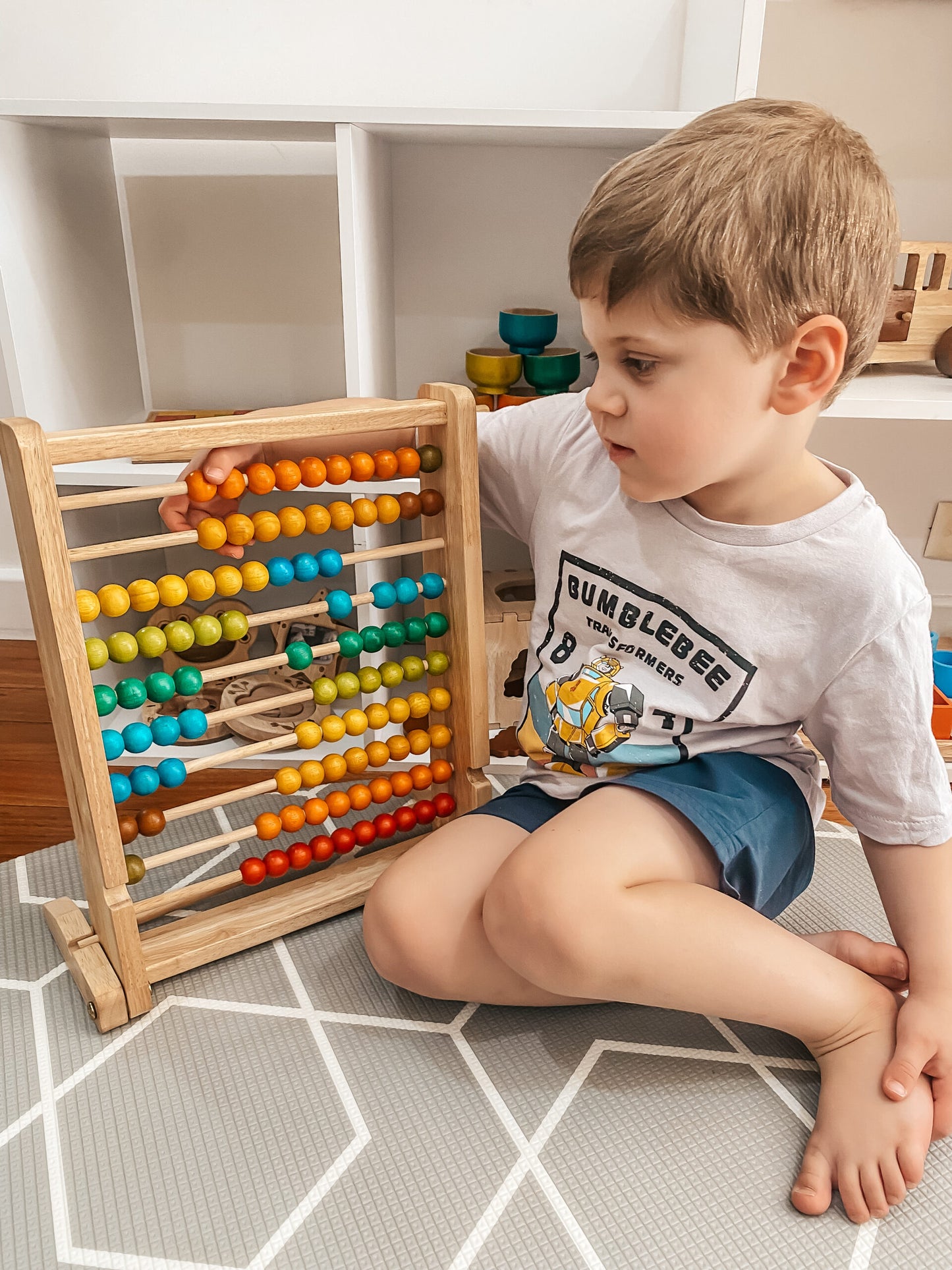 Child playing with a colorful abacus on a tiled floor.
