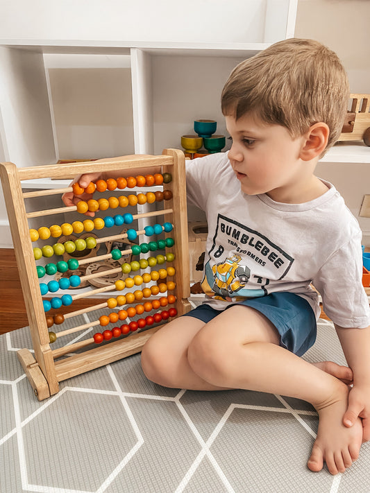 Child playing with a colorful abacus on a tiled floor.